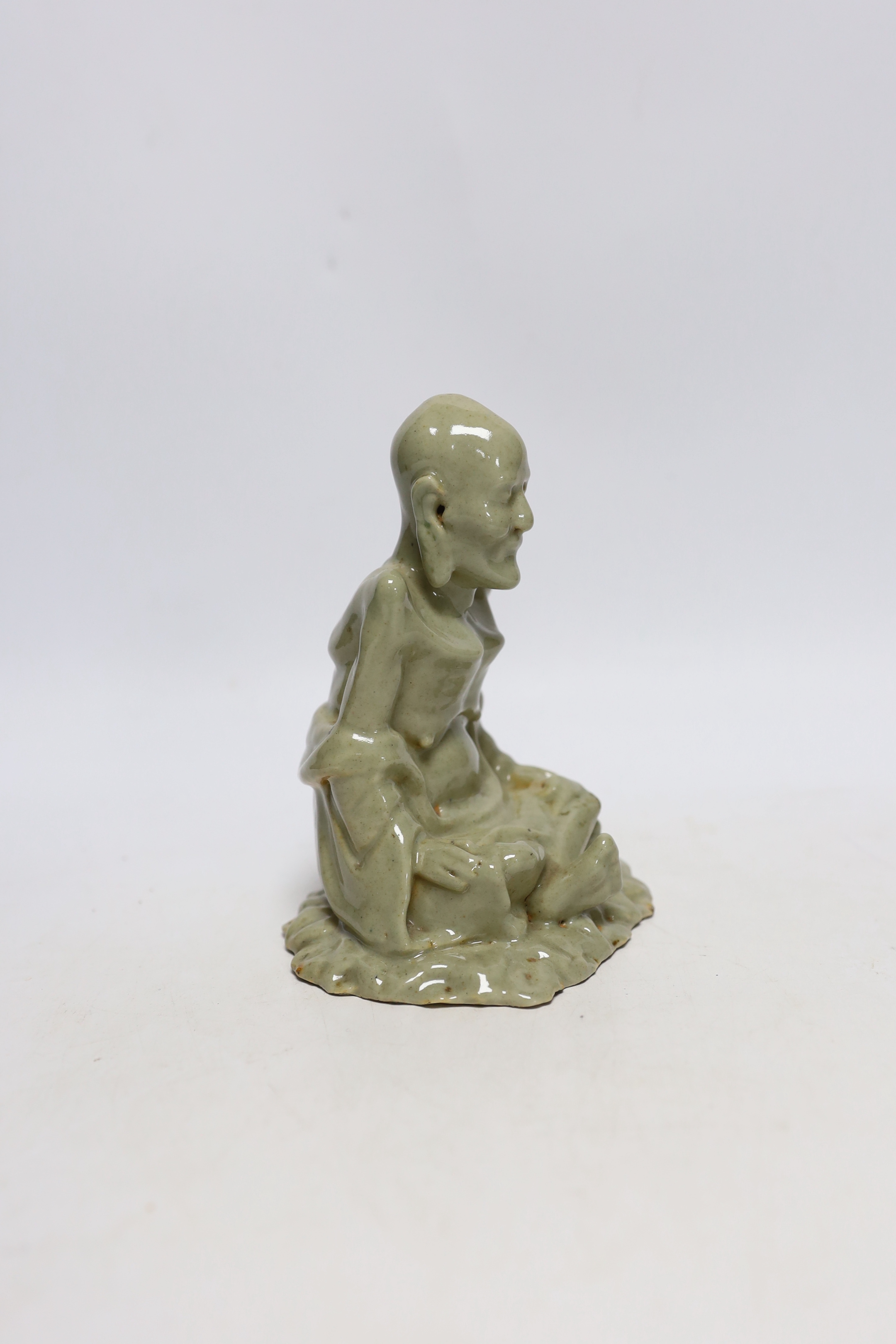 A Chinese celadon glazed figure of Laozi, 18th / 19th century, cross-legged and seated on leaves, 15cm high